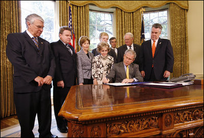 President George W. Bush signs H.J. Res. 93, the Renewal of Import Restrictions on Burma and H.R. 3890, the Tom Lantos Block Burmese JADE Act of 2008, Tuesday, July 29, 2008 in the Oval Office of the White House. President Bush was joined during the signings by, from left, Rep. Don Manzullo, R-Ill.; Rep. Chris Smith, R-N.J.; Mrs. Laura Bush, Annette Lantos, widow of Rep. Tom Lantos; Lantos grandson, Shiloh Tilleman; Rep.Rush Holt, D-N.J.; Rep. Joe Pitts, R-Pa.; and Rep. Peter King, R-N.Y.