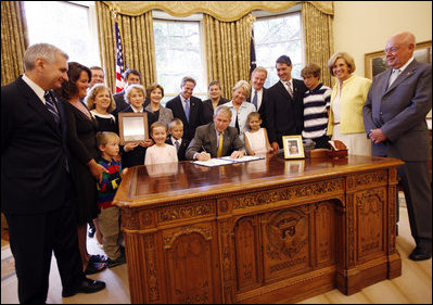 President George W. Bush signs the Caroline Pryce Walker Conquer Childhood Cancer Act of 2008 Tuesday, July 29, 2008, in the Oval Office of the White House. President Bush is joined at his desk by Mrs. Laura Bush, HHS Secretary Mike Leavitt, the Lewis family, the Adams family, the Haight family, the Rech family, and Congressional representatives Sen. Jack Reed D-RI; Minnesota Senator Norm Coleman; Rep. Deborah Pryce R-OH; and Rep. Chris Van Hollen D-MD; and CureSearch's Dr. Gregory Reaman. 