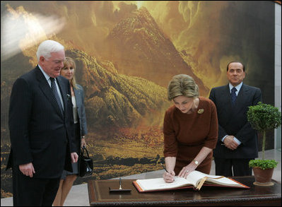 Mrs. Laura Bush signs the guest book Oct. 13, 2008 at the National Gallery of Art in Washington as Italian Prime Minister Silvio Berlusconi waits to sign as well. At left is Mr. Rusty Powell, Director of the National Gallery of Art, who led the tour. The Mt. Vesuvius mural is one of the backdrops for the exhibit.