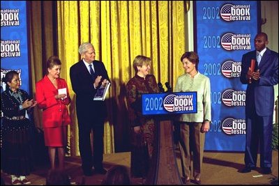Laura Bush welcomes Ludmila Putina, wife of Vladimir Putin, President of the Russian Federation, to the Second Annual National Book Festival Saturday, October 12, 2002 in the East Room of the White House. Standing with the First Ladies on stage are, left to right, Native American poet Lucy Tapahoso, writer Mary Higgins Clark, Librarian of Congress James Billington, and NBA player Jerry Stackhouse. White House photo by Susan Sterner.