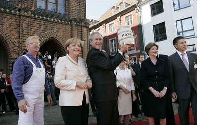 Standing with German Chancellor Angela Merkel, President George W. Bush holds up a ceremonial gift of a barrel of herring in Stralsund, Germany, Thursday, July 13, 2006. Mrs. Bush is pictured at the right.