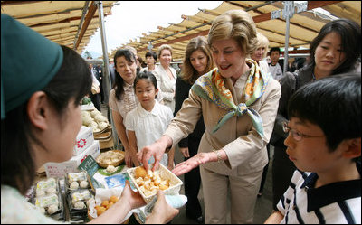 Mrs. Laura Bush tastes a sampling of the food at the Hokkaido Marche farmer's market in Makkari Village Tuesday, July 8, 2008, as part of the G-8 Spouses Program. The small village on the northern Japanese island of Hokkaido is known for its lilies and its potatoes, and the market, organized especially for the occasion of the G-8 Summit, showcased locally grown produce.