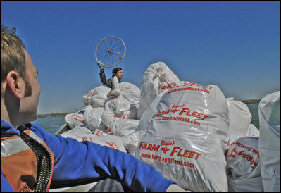 Chad Pregracke, founder of Living Lands and Waters, holds up a bicycle wheel found on the banks of the Potomac River Thursday, April 13, 2005, as White House Intern Casey Verst watches from behind a mountain of collected trash. 