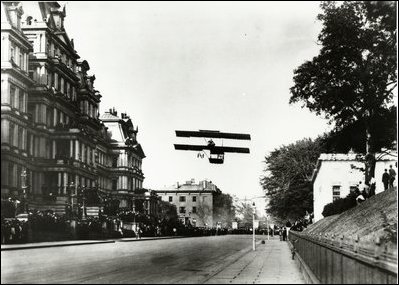 Shown here taking off from West Executive Avenue in 1910, pioneer aviator Claude Graham-White was the first to land a lighter-than-air craft on a street in any city in the world. He had come to lunch with the Secretary of War, and talk about the defense advantages of aeroplanes.