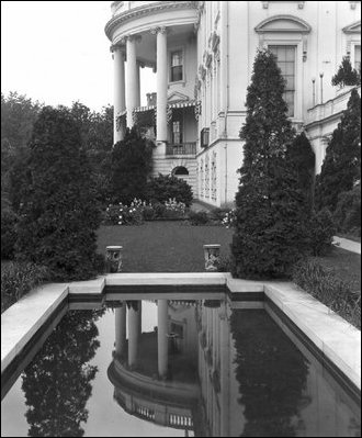 The South Portico is reflected in the surface of the East Garden pond on an overcast day, c. 1910.