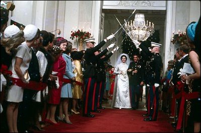 As part of the wedding festivities, President Johnson's daughter, Lynda, and Charles Robb walk under swords into the Cross Hall.