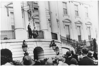 President Hoover waves to crowds at the 1929 Easter Egg Roll from the balcony of The White House. First Lady Lou Hoover, who introduced maypole and folk dancing activities to the event, smiles beside him. 