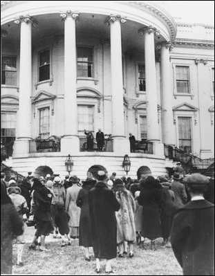 Three years later, in a similar photo, First Lady Lou Hoover waves at the gathering crowd for the White House Easter Egg Roll. President Hoover stands beside her. 