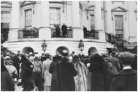 Three years later, in a similar photo, First Lady Lou Hoover waves at the gathering crowd for the White House Easter Egg Roll. President Hoover stands beside her. 