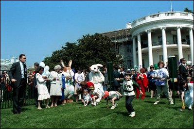 Former President Bush blows a whistle to start an egg roll race at the 1989 White House Easter Egg Roll while First Lady Barbara Bush smiles at the children participating.