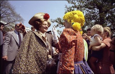 Mrs. Ford greets a clown at the 1976 White House Easter Egg Roll while President Ford watches in the background.