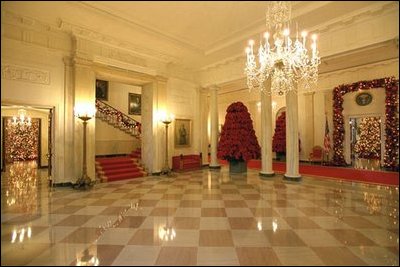 Entrances to both the East Room and the State Dining Room from the Cross Hall are surrounded by garlands full of large pine cones, red glass balls, red icicles and red pepper berries.