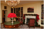 Silver containers filled with red carnations adorn the tables in the Library. The fireplace mantle is decorated with traditional green garland, accented with glass bulbs and red bows.