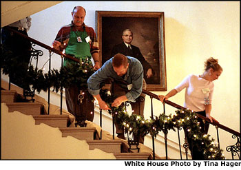  Under the watchful gaze of Harry S. Truman's portrait, volunteers Mike Bickley (left), David Padua (center) and Samantha Rutledge hang garland on the Grand Staircase, which leads from the Grand Foyer up to the President's residence. White House photo by Tina Hager.