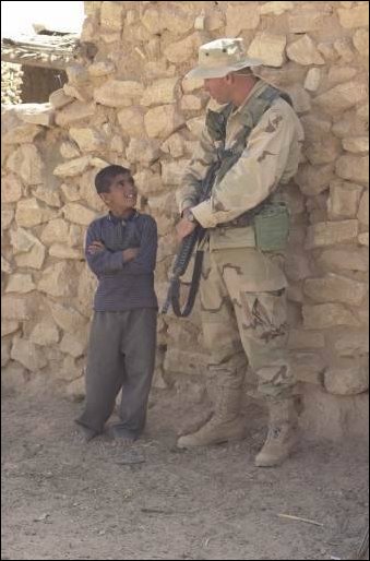 A soldier from the 422nd Civil Affairs Battalion speaks with a boy, while bags of rice and wheat are delivered to a village near the city of Najaf in central Iraq on April 04, 2003, during Operation Iraqi Freedom. (DoD photo by Staff Sgt. Kevin P. Bell, U.S. Army.) 