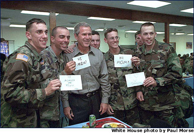 Photo of the President with soldiers holding signs that say "Hi, Mom." White House photo by Paul Morse.