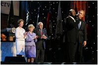President George W. Bush puts his arm around Singer Bebe Winans as he sings 'God Bless America' during the 'Saluting Those Who Serve' event at the MCI Center in Washington, D.C., Tuesday, Jan. 18, 2005. Also pictured are, from left, Laura Bush, Lynne Cheney, and Vice President Dick Cheney.
