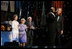 President George W. Bush puts his arm around Singer Bebe Winans as he sings 'God Bless America' during the 'Saluting Those Who Serve' event at the MCI Center in Washington, D.C., Tuesday, Jan. 18, 2005. Also pictured are, from left, Laura Bush, Lynne Cheney, and Vice President Dick Cheney.