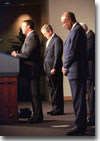 President George W. Bush bows his head as Rep. J.C. Watts, Jr. (R.-Okla.) leads a prayer before the swearing-in ceremony for Rod Paige, right, as Secretary of Education in the Barnard Auditorium at the Department of Education Jan. 24, 2001. White House photo by Eric Draper