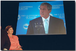 Laura Bush looks on in the audience as President George W. Bush is displayed on a giant screen monitor during his speech at the 69th Conference of Mayors in Detroit, Michigan, Monday, June 25, 2001. White House photo by Eric Draper.