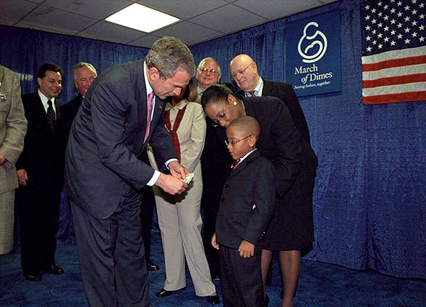 After presenting President George Bush with a pair of boots, March of Dimes Ambassador Justin Lamar Washington gives the President a dollar to help with contributions to the Afghan children during the organizations' Washington D. C. event Oct. 12. White House photo by Tina Hager.