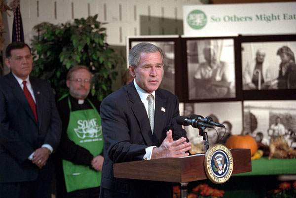 Urging Americans to give of themselves during this holiday season, President George W. Bush addresses volunteers and media at So Other Might Eat interfaith charity in Washington, D. C., Nov. 20. Preparing breakfast and lunch, the programs serves more than 300,00 meals to homeless each year. White House photo by Tina Hager.