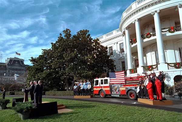 Accompanied by firemen and other distinguished guests, President George W. Bush speaks during a ceremony held to honor the gift of a new firetruck for city of New York on the South Lawn Dec. 19. Donated by the state of Louisiana, the "Spirit of Louisiana," will replace one of the 35 firetrucks that were destroyed in the Sept. 11 attacks. Standing with the President is Louisiana Governor Mike Foster, Louisiana Representative Hunt Downer, and Ronald Goldman. White House photo by Eric Draper.