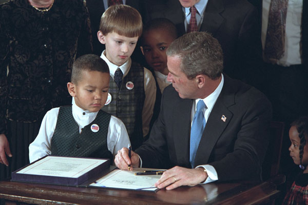 With the help from some new friends, President George W. Bush signs legislation promoting safe and stable families at the White House Jan. 17, 2002. "The legislation reaffirms our country's commitment to helping children grow up in secure and loving families by encouraging adoption," said the President during the ceremony. White House photo by Paul Morse.