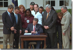 President George W. Bush signs the Job Creation and Worker Assistance Act of 2002 during a live radio address in the Rose Garden March 9, 2002. On hand for the signing were Senators Trent Lott (far left) and Tom Daschle (second from left) and Speaker of the House Dennis Hastert (standing to right of the President). "We're seeing some encouraging signs in the economy, but we can't stand by and simply hope for continued recovery," said President Bush. "We must work for it." White House photo by Eric Draper.
