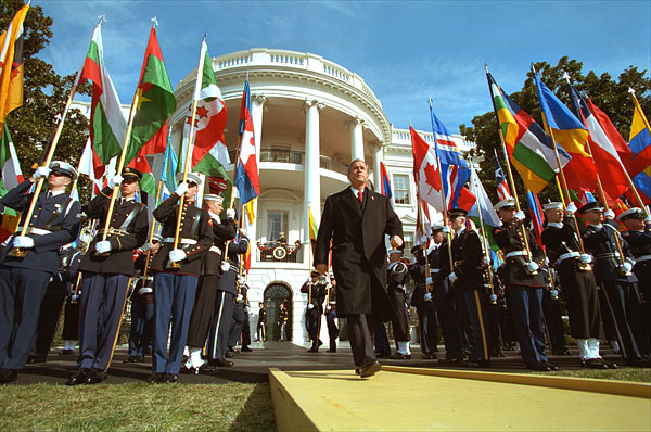 Flying flags from countries contributing to the fight against terrorism, President George W. Bush approaches the podium on the six-month anniversary of the September 11th Attacks on the South Lawn. "We have come together to mark a terrible day, to reaffirm a just and vital cause, and to thank the many nations that share our resolve and will share our common victory," said the President in his remarks. White House photo by Paul Morse.