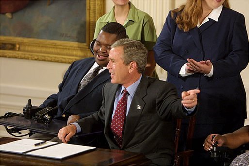 Sitting with William LeRon Jackson of Mississippi, left, President George W. Bush reacts to the audience during the signing of the proclamation that marks the 12th Anniversary of the Americans with Disabilities Act in the East Room Friday, July 26. White House photo by Paul Morse.