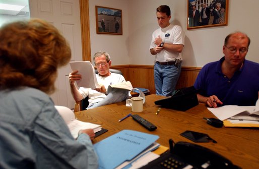 President George W. Bush reads over paperwork during a White House staff meeting inside a telecommunications trailer at the Bush Ranch in Crawford, Texas, Friday, Aug. 9, 2002. From left are Staff Secretary Harriet Miers, personal assistant Blake Gottesman and Deputy Chief of Staff Joe Hagin. White House photo by Eric Draper.