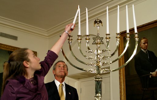 President George W. Bush watches as Daniella Wald, 12, lights one of the candles on the Menorah Wednesday, Dec 4 in the White House. President Bush presented one of the lighted candles to Daniella Wald, who lit the first three candles, and she presented the lighter candle to her sister, Alexandra Wald, 15, who lit the other three. Both of the girls are from Manhattan, and their father, Victor Wald, was killed in the Sept. 11 attacks on the World Trade Center. White House photo by Paul Morse.