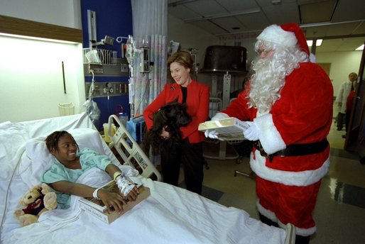 Laura Bush is accompanied by her Scottish Terrier, Barney, and Santa Claus as she visits Brittanie Morris at the Children's National Medical Center in Washington, D.C., Thursday, December 12, 2002. After spending time with children on the neurology and orthopedic units, Mrs. Bush hosted the annual children's Christmas program, during which she debuted a video tour of the White House Christmas decorations from Barney's perspective. White House photo by Susan Sterner.