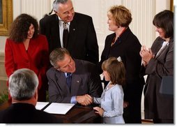 After signing a proclamation recognizing October as Domestic Violence Month, President George W. Bush shakes hands with Monique Blais, 7, the young artist who designed the Stop the Violence postage stamp in the East Room Wednesday, Oct. 8, 2003.  White House photo by Tina Hager