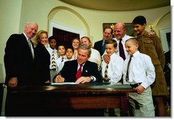 President George W. Bush signs the Adoption Promotion Act of 2003 in the Roosevelt Room December 2, 2003. Pictured with the President are the Chris and Diana Martin family. Their children are Katrina, 13, Ashley, 12, T.J., 11, Kyle, 10, Travis, 10, Dakota, 8, and Terrance, 7. Also pictured are Congressman James Oberstar, far left, Senator Mary Landrieu, and at back right, Congressman Dave Camp.  White House photo by Eric Draper