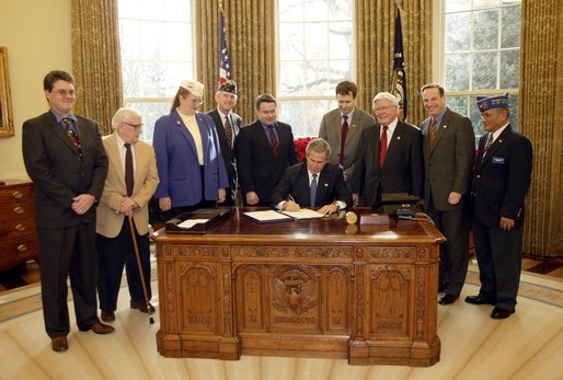 President George W. Bush signs H. R. 2297, the Veterans Benefits Act of 2003, in the Oval Office Tuesday, Dec. 16, 2003. The act expands the benefits program for veterans and their surviving spouses. In attendance are, from left: veterans Dave Thornton of Haymarket, Va.; Charles Stenger of Bethesda, Md.; Carol Near of East Moline, Ill.; Congressman Rob Simmons, R-Conn.; Congressman Chris Smith, R-N.J.; Congressman Lane Evans, D-Ill.; Congressman Henry Brown, R-S.C.; Congressman Bob Filner, D-Calif.; and veteran Guillermo Rumingan of Arlington, Va. White House photo by Paul Morse.