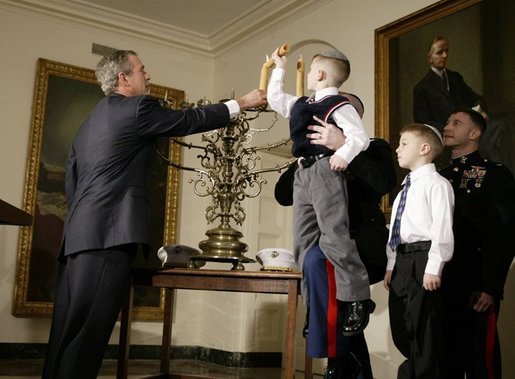 President George W. Bush helps Jacob Murphy light a menorah along with his father Captain Neil Murphy Jr. Wednesday afternoon December 22, 2003 at the White House. White House photo by Paul Morse