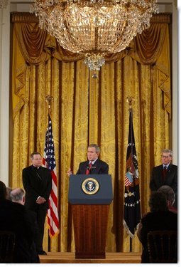 President George W. Bush addresses The National Catholic Educational Association in the East Room Friday, Jan. 9, 2004. Pictured with the President are Bishop Gregory Aymond of Austin, Texas, left and Michael Guerra, President of the NCEA.  White House photo by Tina Hager
