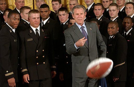 After being presented with a team-signed football, President George W. Bush throws it to an aide during the presentation of the Commander-In-Chief Trophy to the U.S. Naval Academy football team in the East Room Monday, April 19, 2004. The trophy is awarded to the Service Academy with the year's best overall record in NCAA football games versus the other academies. White House photo by Tina Hager.