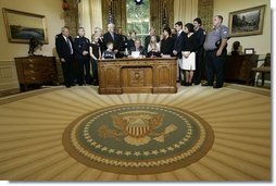 President George W. Bush delivers a Live Radio Address surrounded by Mrs. Bush and families of victims of 911 in the Oval Office, Saturday, Sept. 11, 2004.  White House photo by Eric Draper