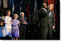 President George W. Bush puts his arm around Singer Bebe Winans as he sings 'God Bless America' during the 'Saluting Those Who Serve' event at the MCI Center in Washington, D.C., Tuesday, Jan. 18, 2005. Also pictured are, from left, Laura Bush, Lynne Cheney, and Vice President Dick Cheney.   White House photo by David Bohrer