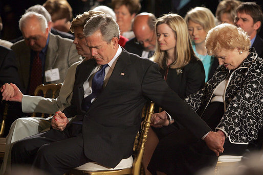 President George W. Bush and Laura Bush holds hands with guests while praying during a ceremony observing the National Day of Prayer in the East Room Thursday, May 5, 2005. White House photo by Krisanne Johnson