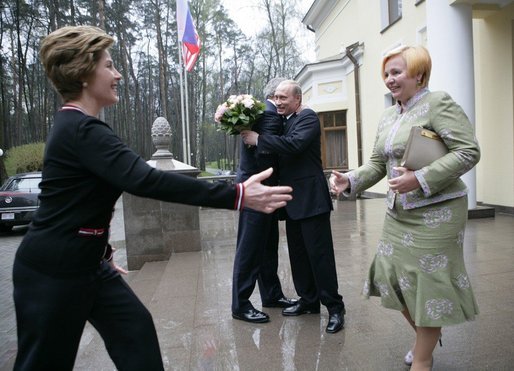 President George W. Bush and Russia President Vladimir Putin embrace in the background as Mrs. Bush reaches out to Lyudmila Putina, Russia's first lady, as the Bushes arrived Sunday, May 8, 2005, at the Putin residence shortly after their arrival in Moscow. White House photo by Eric Draper