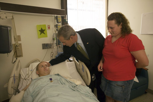 President George W. Bush pats the head of Pvt. 2nd Class Bart Tucker of Sioux City, Iowa, Friday, July 1, 2005, while his wife Heather looks on. The President visited the soldier at Walter Reed Army Medical Hospital, where he awarded Pvt. Tucker a Purple Heart for injuries received while serving in Operation Iraqi Freedom. White House photo by Eric Draper