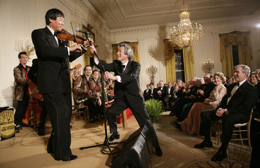 President George W. Bush watches as Japanese Prime Minister Junichiro Koizumi adjusts the microphone for country music entertainer Shoji Tabuchi Thursday evening, June 29, 2006 in the East Room of the White House, during the entertainment following the official dinner in honor of Koizumi’s visit to the United States. White House photo by Eric Draper