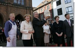 Standing with German Chancellor Angela Merkel, President George W. Bush holds up a ceremonial gift of a barrel of herring in Stralsund, Germany, Thursday, July 13, 2006. Mrs. Bush is pictured at the right.  White House photo by Eric Draper