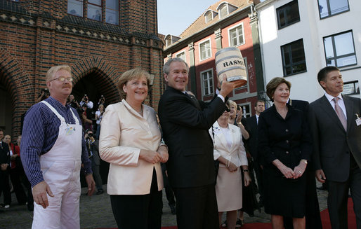 Standing with German Chancellor Angela Merkel, President George W. Bush holds up a ceremonial gift of a barrel of herring in Stralsund, Germany, Thursday, July 13, 2006. Mrs. Bush is pictured at the right. White House photo by Eric Draper