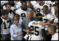 President George W. Bush and Laura Bush are surrounded by members of the New Orleans Saints football team Tuesday, Aug. 29, 2006, as they point out the name of Saints star rookie running back Reggie Bush, when the team met President Bush at the New Orleans Airport to pose for a team photo. White House photo by Eric Draper