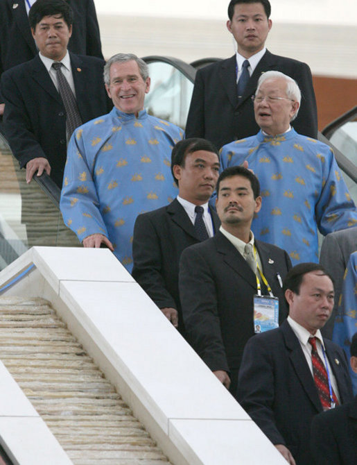 President George W. Bush takes an escalator at the National Convention Center in Hanoi, en route to APEC Island for the 2006 official portrait. To his right is Morris Chang, the APEC representative from Taiwan. White House photo by Eric Draper